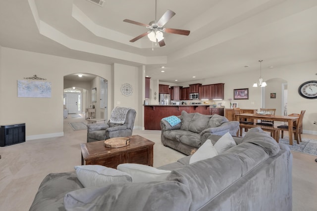 living room with light colored carpet, ceiling fan with notable chandelier, and a raised ceiling