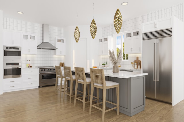 kitchen featuring backsplash, light hardwood / wood-style flooring, premium appliances, wall chimney range hood, and white cabinetry