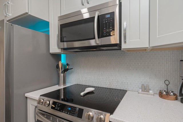 kitchen featuring white cabinets, stainless steel appliances, light stone countertops, and backsplash