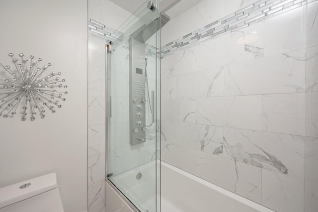 bathroom featuring toilet and shower / bath combination with glass door