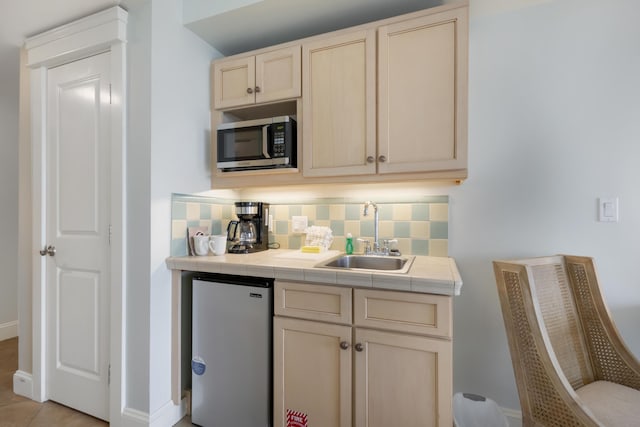 bar with fridge, sink, tasteful backsplash, light tile flooring, and tile counters