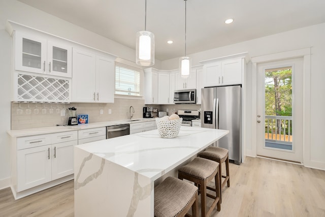 kitchen with appliances with stainless steel finishes, a center island, tasteful backsplash, light hardwood / wood-style flooring, and pendant lighting