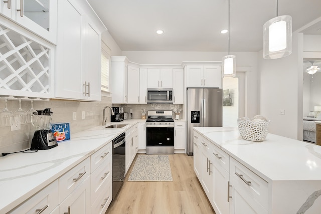 kitchen with white cabinets, sink, hanging light fixtures, stainless steel appliances, and light hardwood / wood-style flooring