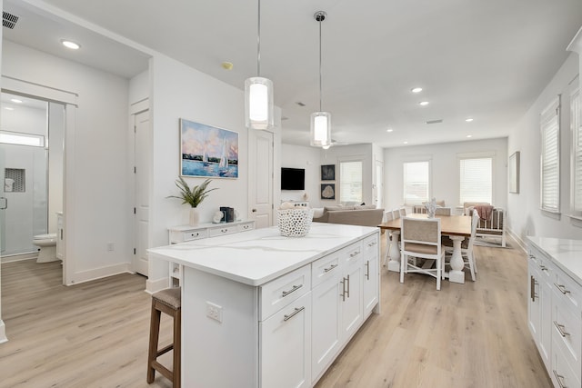 kitchen with a center island, white cabinets, light hardwood / wood-style floors, a kitchen breakfast bar, and pendant lighting