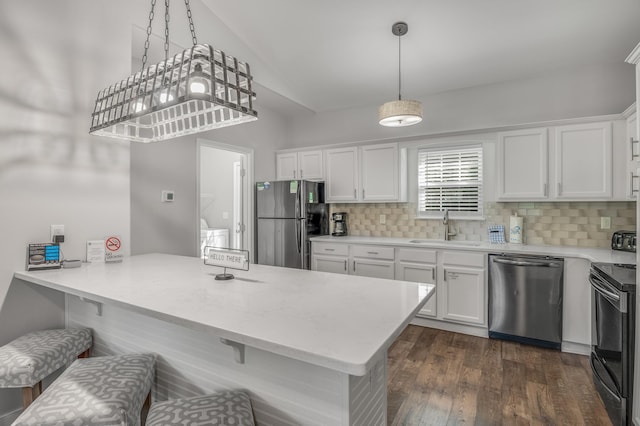 kitchen with appliances with stainless steel finishes, a kitchen bar, sink, white cabinetry, and dark wood-type flooring