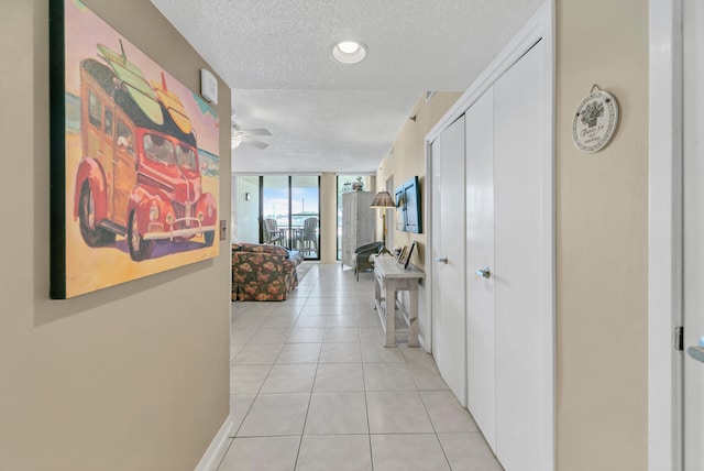 corridor with floor to ceiling windows, a textured ceiling, and light tile floors