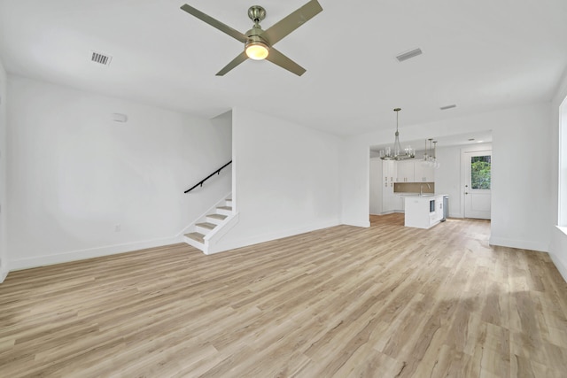 unfurnished living room with ceiling fan with notable chandelier, light wood-style flooring, stairway, and visible vents