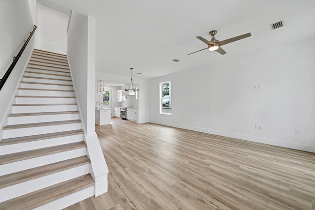 unfurnished living room featuring ceiling fan with notable chandelier and light wood-type flooring