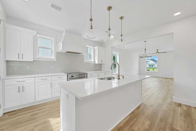 kitchen featuring a kitchen island with sink, sink, white cabinets, and stainless steel range with electric cooktop