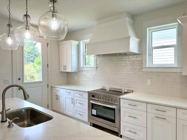 kitchen with sink, high end stove, decorative light fixtures, white cabinets, and custom range hood