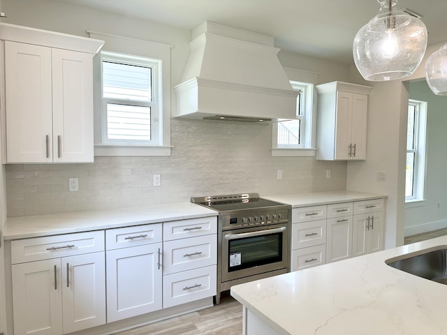 kitchen with electric range, white cabinets, custom range hood, light stone countertops, and pendant lighting