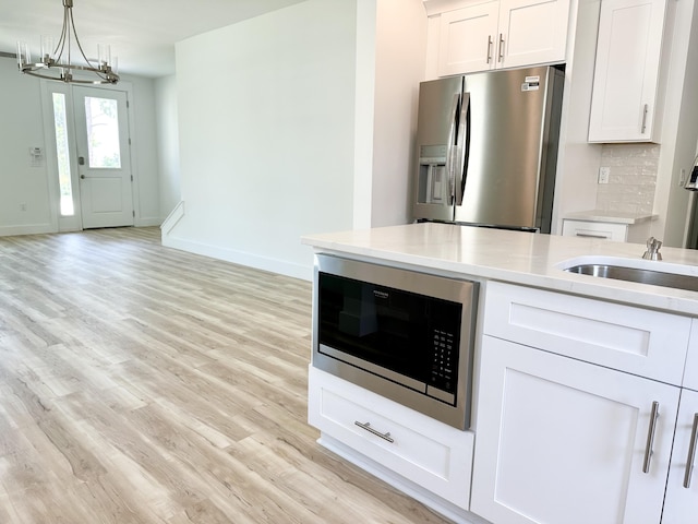 kitchen with pendant lighting, stainless steel refrigerator with ice dispenser, light countertops, white cabinets, and built in microwave