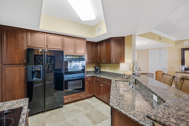 kitchen featuring kitchen peninsula, a kitchen breakfast bar, sink, black appliances, and dark stone countertops