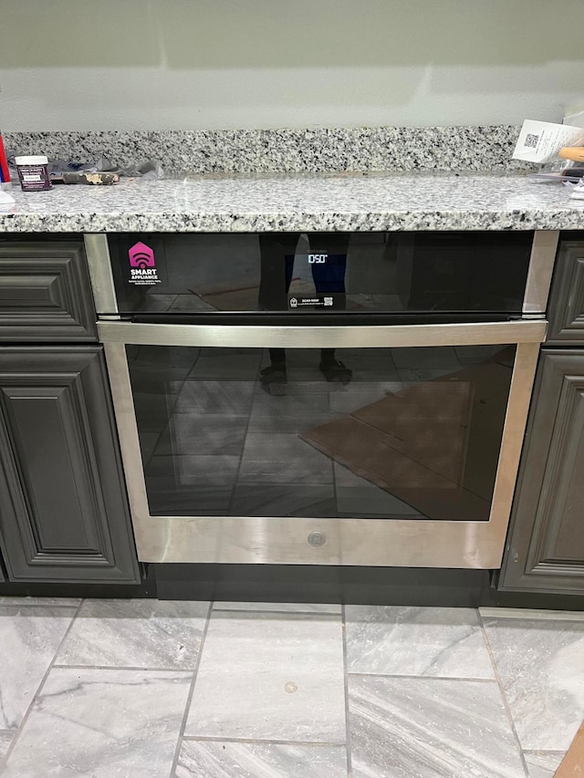 interior details with stainless steel oven, light stone countertops, and light tile patterned floors