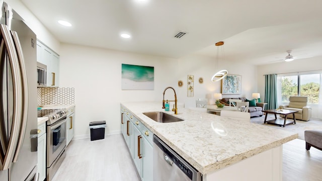 kitchen with pendant lighting, sink, stainless steel appliances, an island with sink, and decorative backsplash