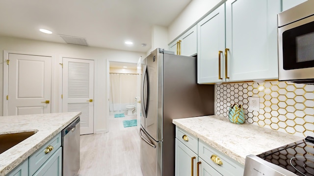 kitchen featuring backsplash, light hardwood / wood-style flooring, light stone countertops, and appliances with stainless steel finishes