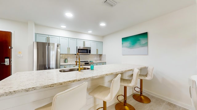 kitchen with appliances with stainless steel finishes, sink, a breakfast bar area, backsplash, and light stone countertops