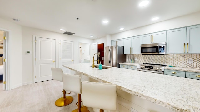 kitchen featuring a breakfast bar, sink, stainless steel appliances, light hardwood / wood-style floors, and decorative backsplash