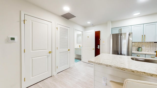 kitchen with tasteful backsplash, stainless steel fridge, light hardwood / wood-style floors, and sink