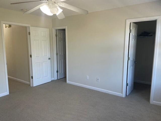 unfurnished bedroom featuring a spacious closet, a closet, ceiling fan, and dark carpet