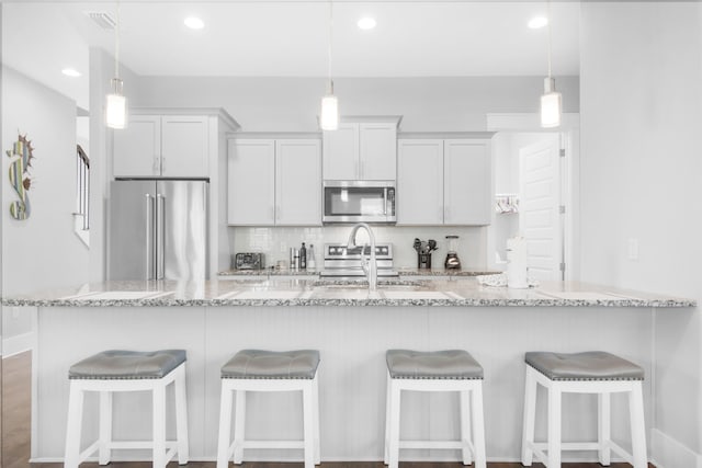 kitchen featuring decorative light fixtures, hardwood / wood-style floors, stainless steel appliances, and light stone countertops