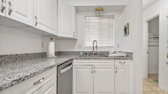 kitchen with light stone counters, white cabinetry, sink, light tile floors, and stainless steel dishwasher