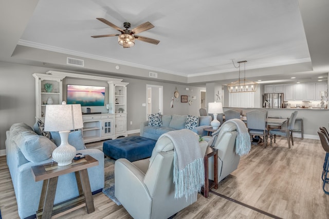 living room with ceiling fan with notable chandelier, light hardwood / wood-style flooring, and a raised ceiling