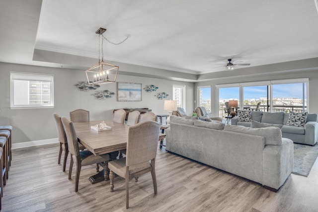 dining space with ceiling fan with notable chandelier, light hardwood / wood-style floors, and a raised ceiling