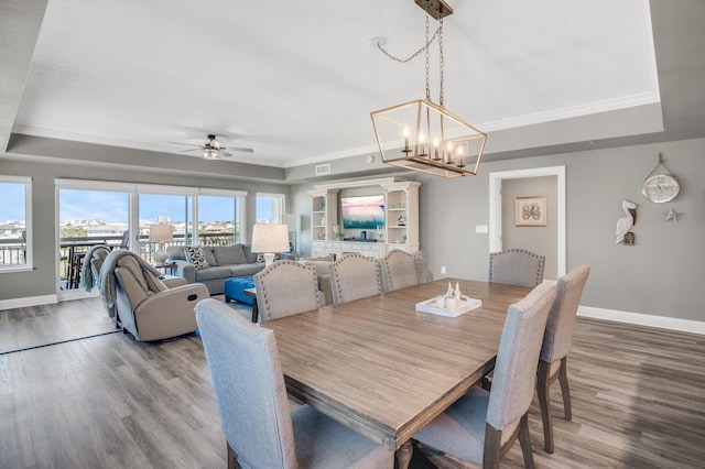 dining space featuring ceiling fan with notable chandelier, hardwood / wood-style floors, crown molding, and a raised ceiling