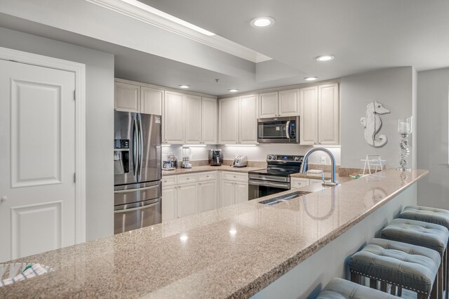 kitchen featuring light stone countertops, kitchen peninsula, stainless steel appliances, white cabinets, and sink