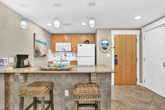 kitchen with hanging light fixtures, white appliances, kitchen peninsula, a breakfast bar, and light tile floors