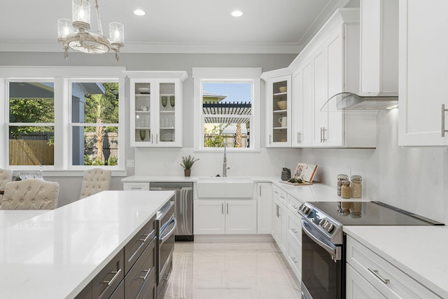 kitchen featuring appliances with stainless steel finishes, wall chimney range hood, white cabinetry, decorative light fixtures, and a wealth of natural light