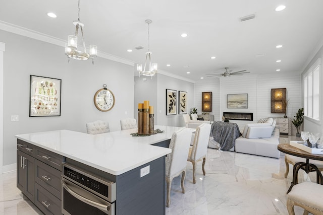 kitchen featuring decorative light fixtures, a large fireplace, ceiling fan with notable chandelier, stainless steel oven, and a center island