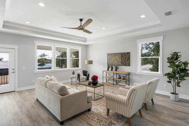 living room with ceiling fan, a wealth of natural light, light wood-type flooring, and a tray ceiling