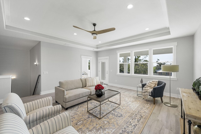 living room featuring light hardwood / wood-style flooring, ceiling fan, and a raised ceiling