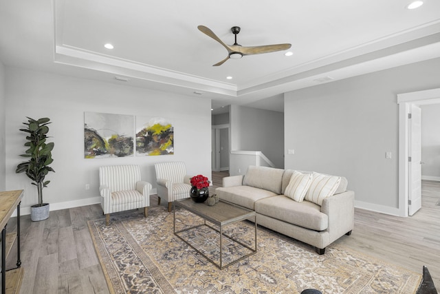 living room featuring ceiling fan, a tray ceiling, and light wood-type flooring