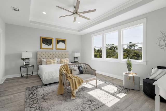 bedroom with light hardwood / wood-style floors, ceiling fan, and a tray ceiling