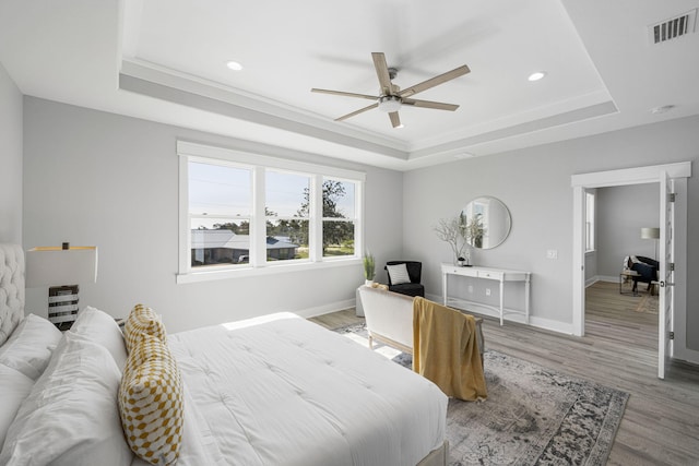 bedroom featuring light hardwood / wood-style flooring, ceiling fan, and a tray ceiling