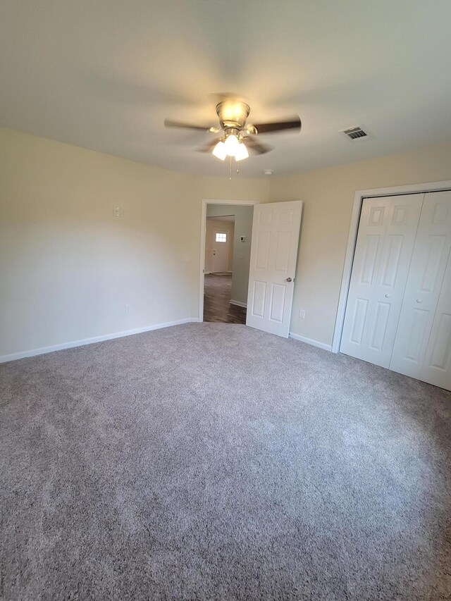 unfurnished bedroom with dark colored carpet, a closet, and ceiling fan