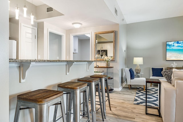 kitchen with light hardwood / wood-style flooring, a kitchen bar, and light stone countertops