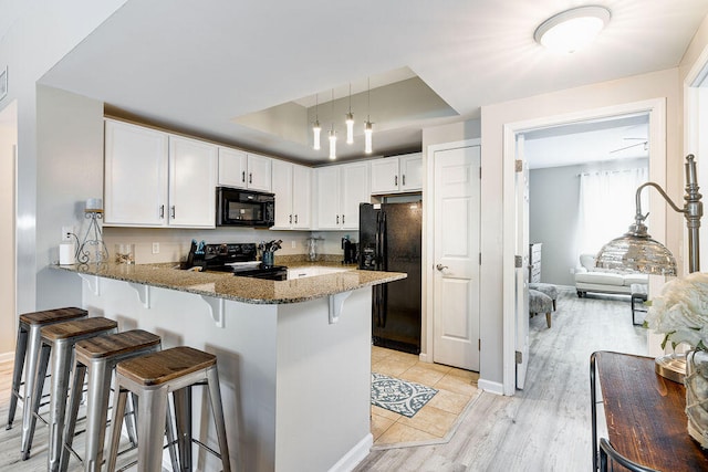 kitchen featuring kitchen peninsula, a kitchen bar, black appliances, a tray ceiling, and dark stone counters