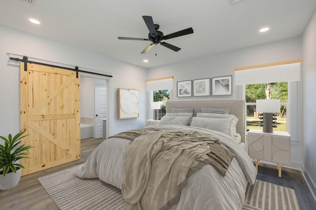 bedroom with ceiling fan, dark wood-type flooring, connected bathroom, and a barn door