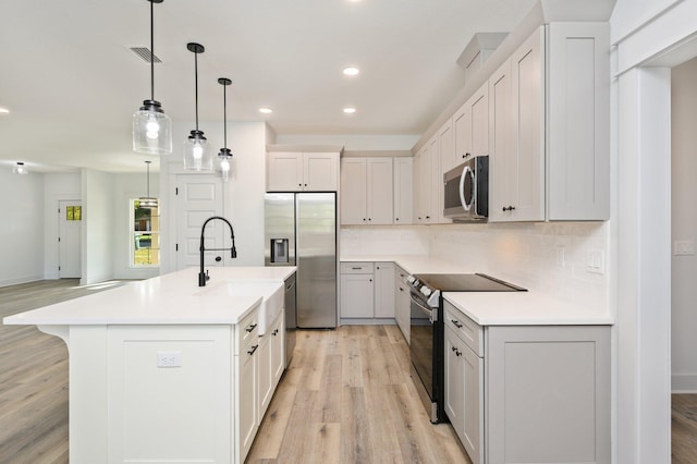 kitchen with appliances with stainless steel finishes, tasteful backsplash, an island with sink, pendant lighting, and light wood-type flooring