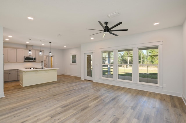 kitchen with decorative light fixtures, ceiling fan, light hardwood / wood-style floors, a kitchen island with sink, and a breakfast bar