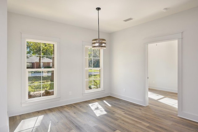 empty room featuring plenty of natural light, light hardwood / wood-style floors, and an inviting chandelier