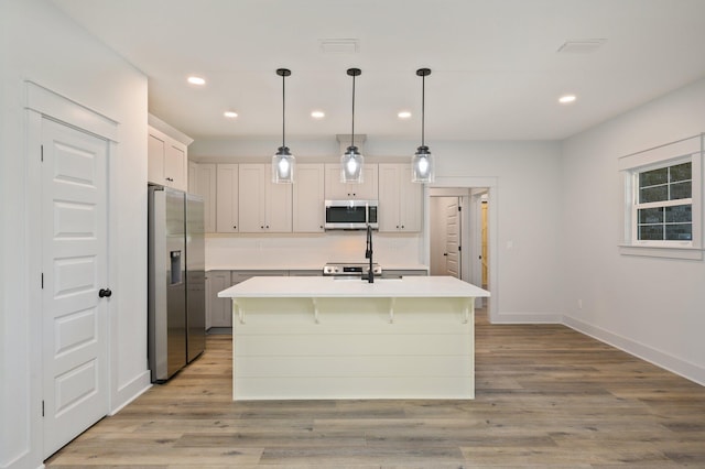 kitchen with appliances with stainless steel finishes, a center island with sink, light wood-type flooring, and hanging light fixtures