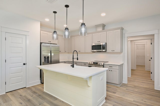 kitchen with hanging light fixtures, light hardwood / wood-style flooring, stainless steel appliances, and a kitchen island with sink