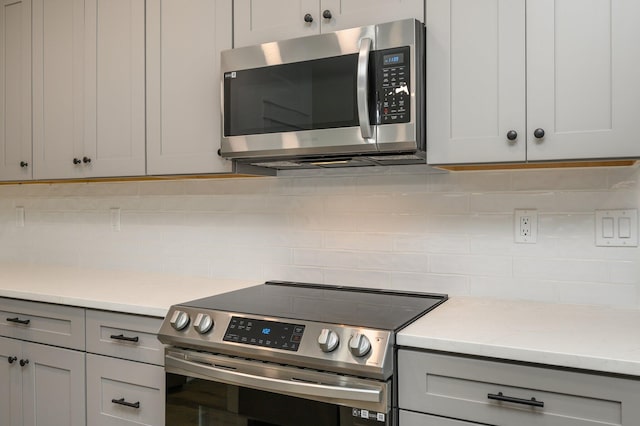 kitchen with appliances with stainless steel finishes, gray cabinets, light stone countertops, and backsplash