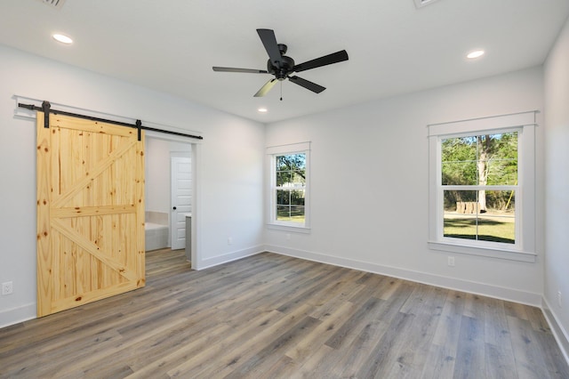 unfurnished bedroom with ensuite bath, a barn door, dark hardwood / wood-style flooring, and ceiling fan