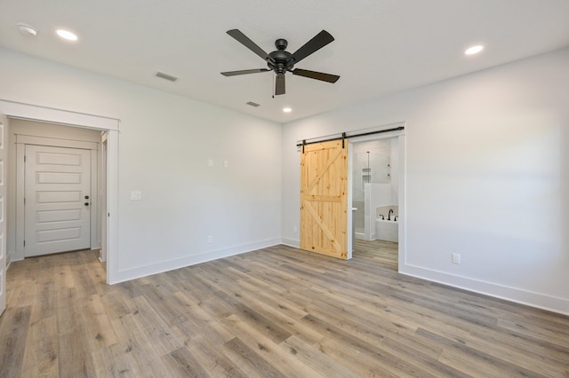 unfurnished bedroom with ceiling fan, light hardwood / wood-style floors, and a barn door